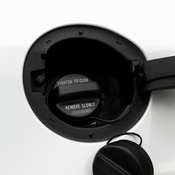 A close-up of a Honda 17670-TR0-A11 Fuel Cap being removed from a white vehicle fuel tank, with printed safety text visible on the cap.