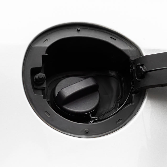 Close-up of a black fuel door cover opened to reveal the fuel filler cap inside a white vehicle body.