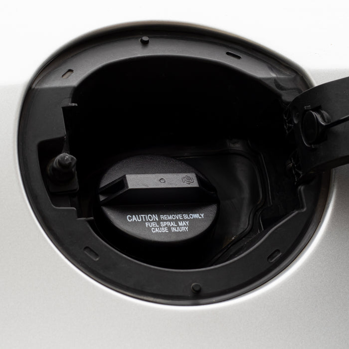 Close-up of a black Toyota 77310-12140 Fuel Cap opening inside a silver vehicle trunk, with printed warning text on the cap.