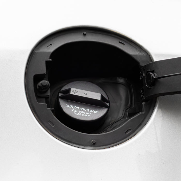 Close-up of a Toyota Lexus Fuel Gas Cap 77310-48020 installed into a white vehicle fuel tank opening, with the fuel cap visible inside and warning text printed on the cap.