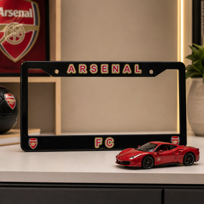 Black Arsenal FC license plate frame with a red car model on a shelf.