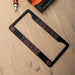 A black license plate frame with Auburn Tigers branding, laid flat on a light wood surface with mounting hardware nearby.