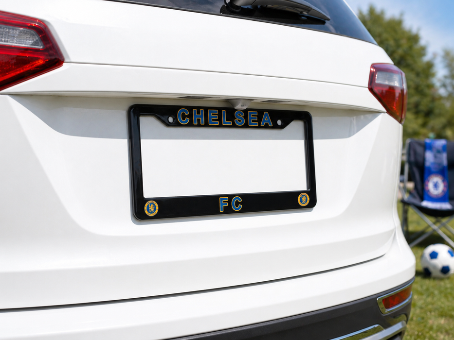White car with a black license plate frame displaying 'CHELSEA FC' on a grassy field.