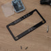 Black license plate frame with 'CHELSEA FC' text on a wooden surface with tools.