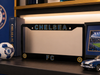 Black Chelsea FC license plate frame on a shelf with football and car model.