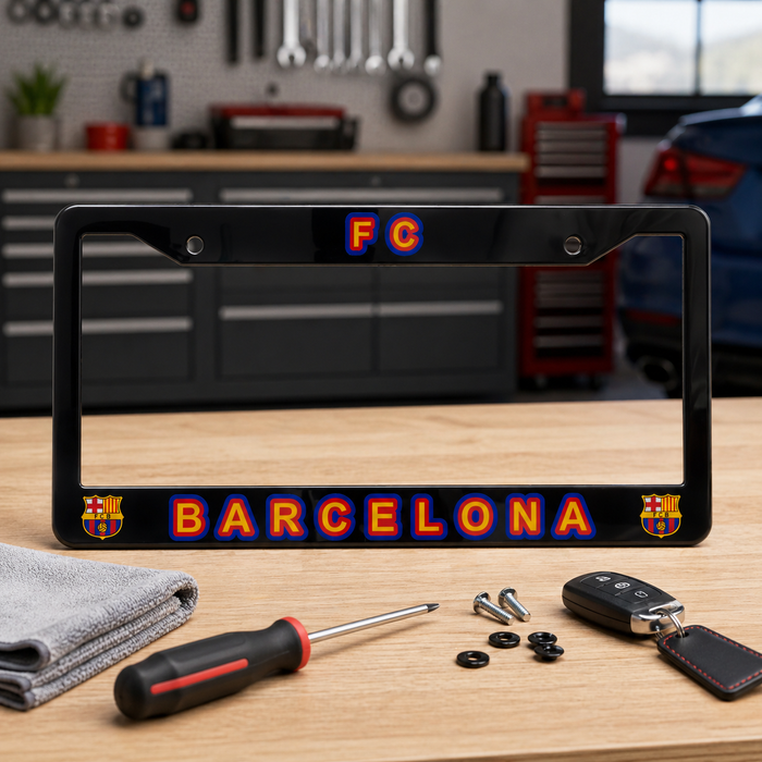 Black license plate frame with FC Barcelona logo on a wooden table in a garage setting.