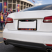 White car with a Barcelona-themed license plate in front of a stadium with fans and flags.
