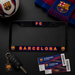 A black license plate frame featuring 'FC BARCELONA' in red and yellow outlined lettering, styled on a dark surface with an FC Barcelona scarf, soccer ball, keys, and tickets.