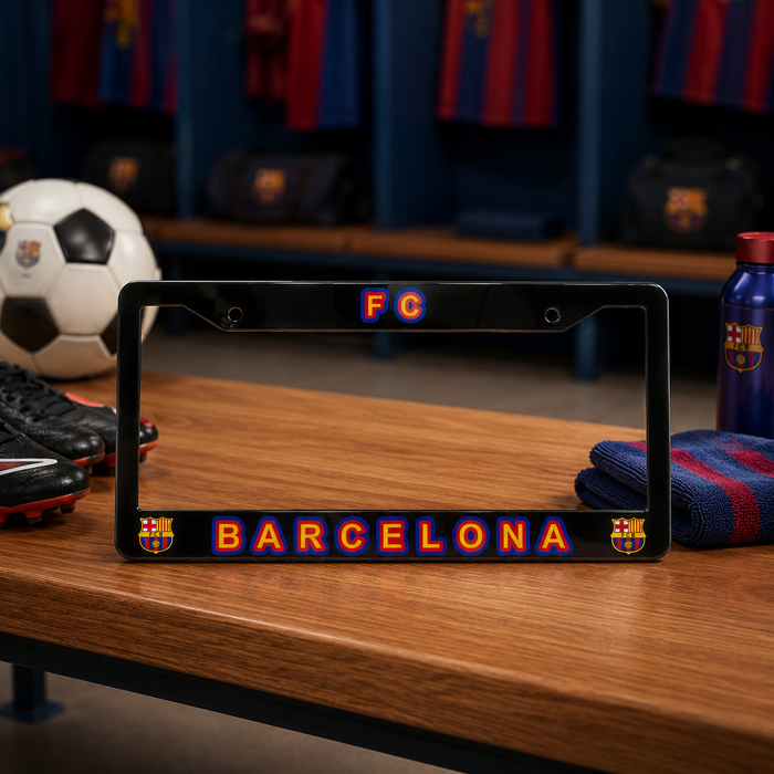 A black license plate frame featuring the FC Barcelona logo and 'BARCELONA' text in red and blue, displayed on a wooden table in a locker room setting with soccer gear in the background.