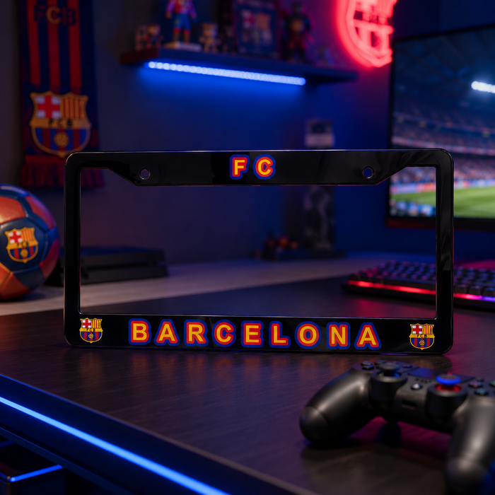 A black license plate frame featuring 'FC' at the top and 'BARCELONA' with FC Barcelona crests at the bottom, displayed on a desk in a gaming room setting.
