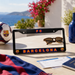 A black license plate frame with 'FC BARCELONA' in red and blue outlined lettering, displayed on a table with a Barcelona scarf, sunglasses, passport, ticket, soccer ball, and a scenic coastal background.