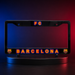 A black license plate frame featuring 'FC BARCELONA' in glowing red and blue lettering, displayed on a circular stand against a blue-to-red gradient studio background.