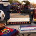 A black license plate frame featuring the FC Barcelona crest and 'FC BARCELONA' in red, yellow, and blue lettering, displayed on a folding table at an outdoor fan event.