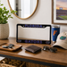 A black license plate frame with 'FLORIDA' and 'GATORS' in blue and orange Florida Gators lettering, styled on a wooden console table with a wallet, sunglasses, keys, a tumbler, and a cap.