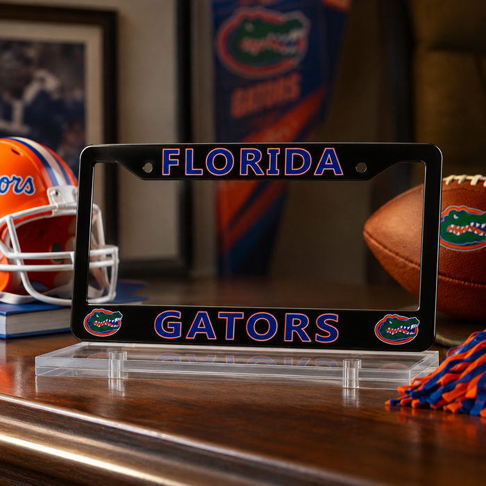 A black Florida Gators license plate frame with blue and orange lettering, displayed on a clear acrylic stand on a wooden table with football-themed decor in the background.