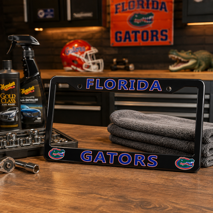 A black Florida Gators license plate frame displayed on a wooden workbench in a garage-like setting. The frame features 'FLORIDA' at the top and 'GATORS' at the bottom in blue letters with a white outline, plus Florida Gators logos in the lower corners.