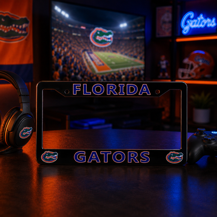 A black Florida Gators license plate frame with blue and orange lettering, displayed on a dark wooden table in a themed room with gaming accessories and a TV showing a football game.