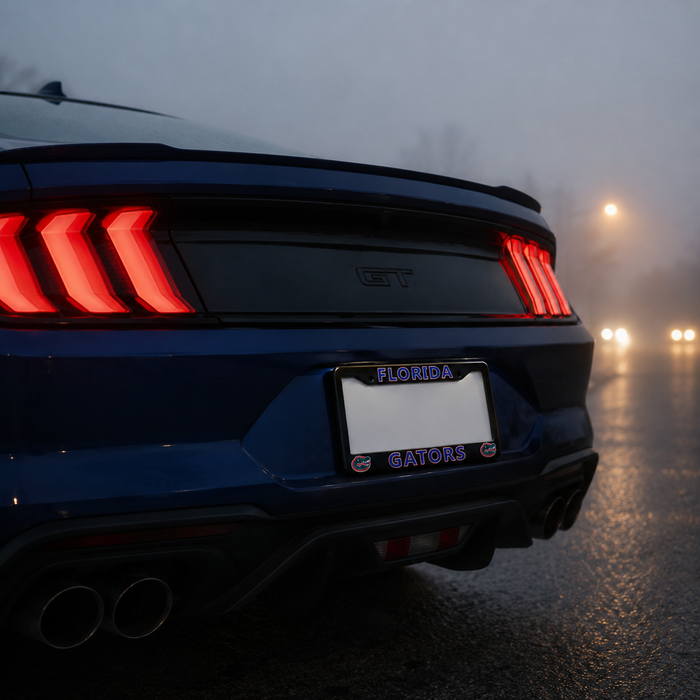 Rear view of a dark blue Ford Mustang GT on a wet road at dusk, with the brake lights illuminated and a Florida Gators license plate frame mounted around the license plate.