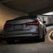 Rear three-quarter view of a matte dark gray sedan parked under a concrete tunnel, showing the back of the car with dual exhausts, a Florida/Gators license plate, and illuminated LED taillights.