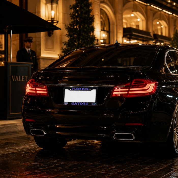 A black luxury sedan photographed from the rear at night on a cobblestone street outside a building with warm lit windows. The car has a Florida license plate with 'GATORS' in blue text.