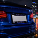 A close-up rear view of a blue car on a wet city street at night, featuring a Florida Gators themed license plate frame with 'FLORIDA' at the top and 'GATORS' at the bottom, flanked by small gator logos.