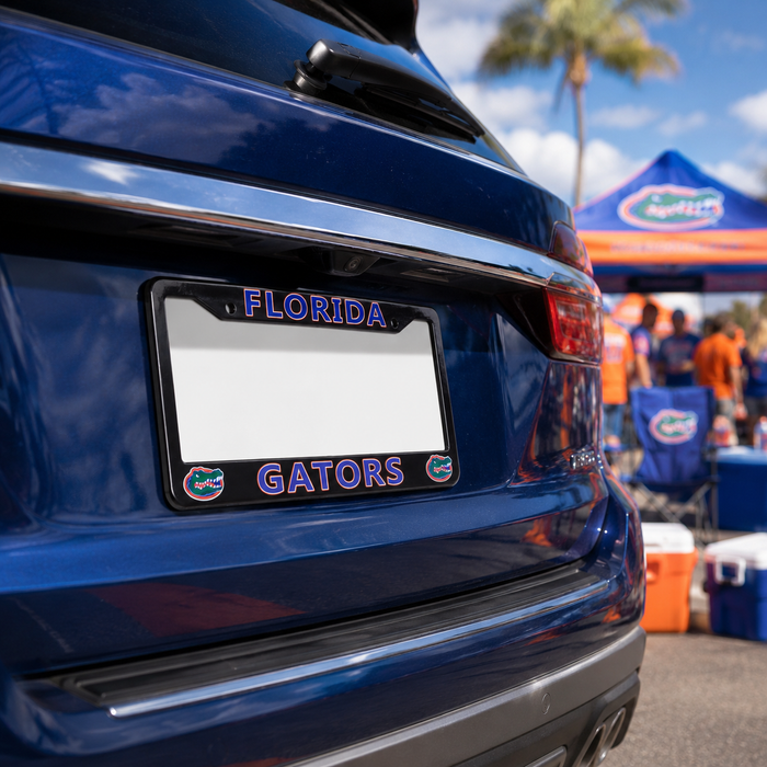 A close-up of a blue car rear bumper showing a Florida Gators license plate frame with purple lettering and alligator logos, set against a blurred outdoor event background with a Florida canopy.