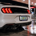 Rear view of a white Ford Mustang with its taillights on and a Florida license plate, parked at a gas station in the rain.
