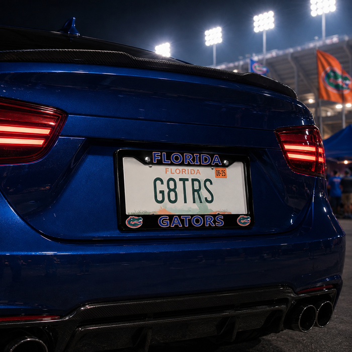 Close-up rear view of a blue car at night with a Florida license plate reading G8TRS and Florida Gators branding on the plate frame, with stadium lights and flags in the background.