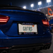 Close-up rear view of a blue car at night with a Florida license plate reading G8TRS and Florida Gators branding on the plate frame, with stadium lights and flags in the background.