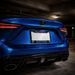 Close-up rear view of a blue Lexus car parked in a parking garage, showing the trunk, license plate frame with Florida Gators text, taillights, and exhaust pipes.