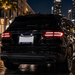 A black luxury SUV photographed from the rear at night on a wet city street, with illuminated taillights, a Florida license plate, and blurred buildings and palm trees in the background.