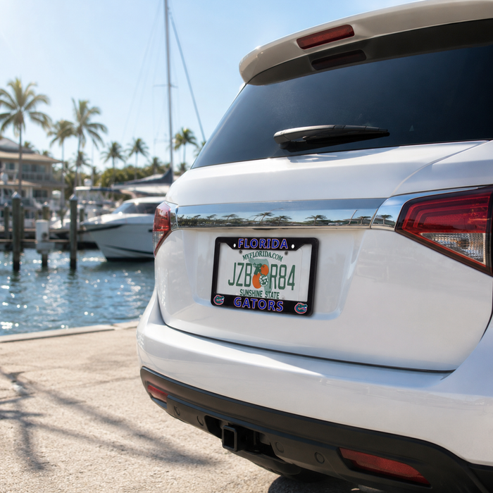 A white SUV rear bumper area parked at a marina, featuring a Florida license plate with a custom black frame that reads 'JZO R84' and 'GATORS' in blue and orange. Palm trees, boats, and water are visible in the background.