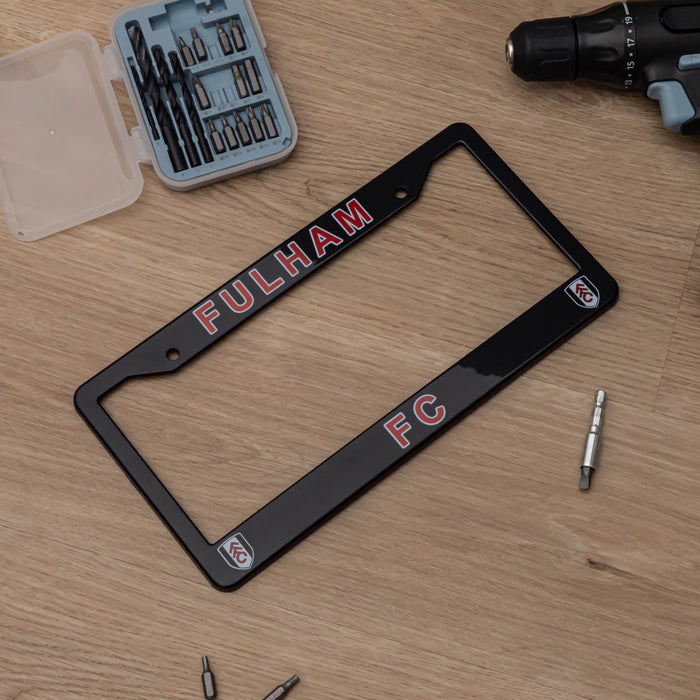 Black license plate frame with 'Fulham FC' text on a wooden surface with tools.