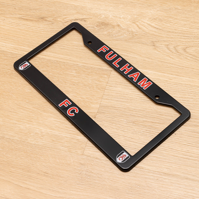Black license plate frame with 'Fulham FC' text on a wooden surface