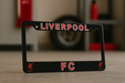 Black license plate frame with 'Liverpool FC' text on a blurred background