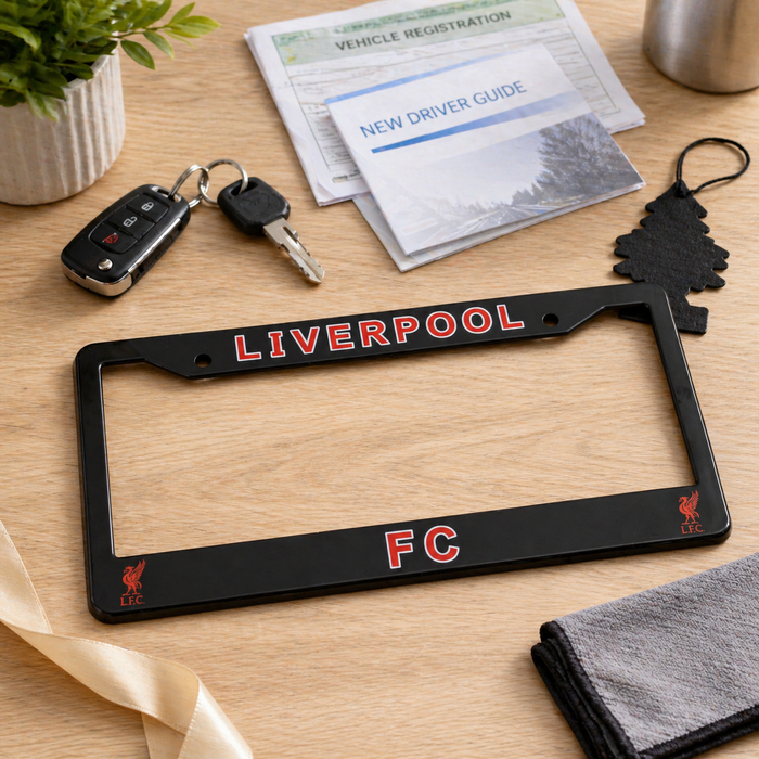Black license plate frame with 'Liverpool FC' on a wooden surface with keys and a driver guide.