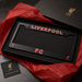 Black license plate frame with 'Liverpool FC' text on a red fabric background