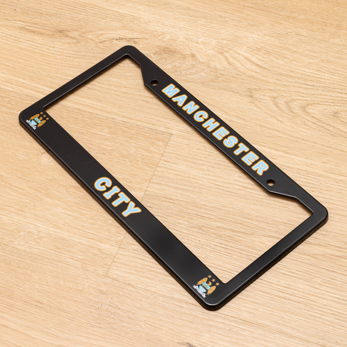 Black license plate frame with 'Manchester City' text on a wooden surface