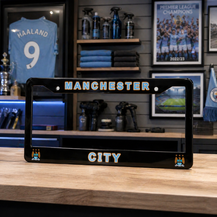 Manchester City-themed license plate on a wooden surface with sports memorabilia in the background.