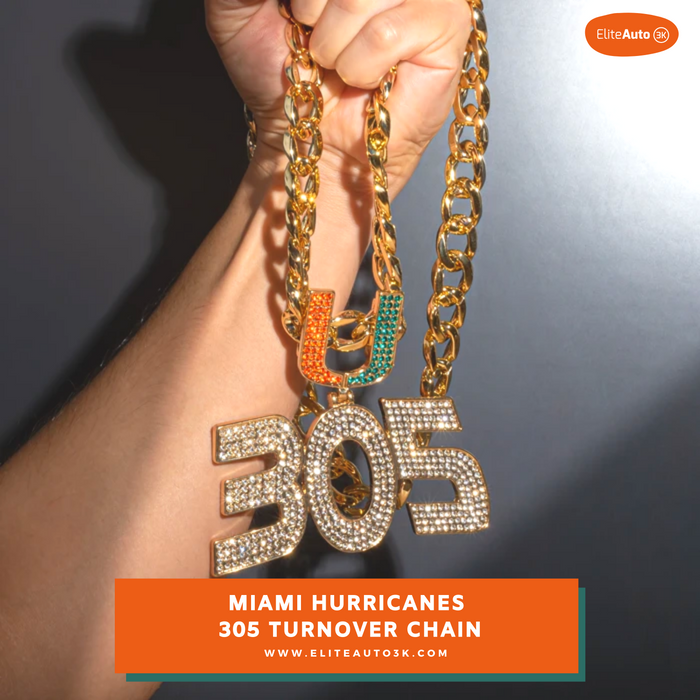 A close-up of a hand holding a gold-tone chain necklace with a large rhinestone-encrusted '305' pendant and a smaller orange and green letter pendant spelling 'UH'. The image has an EliteAuto branding mark and a text banner at the bottom reading 'MIAMI HURRICANES 305 TURNOVER CHAIN'.
