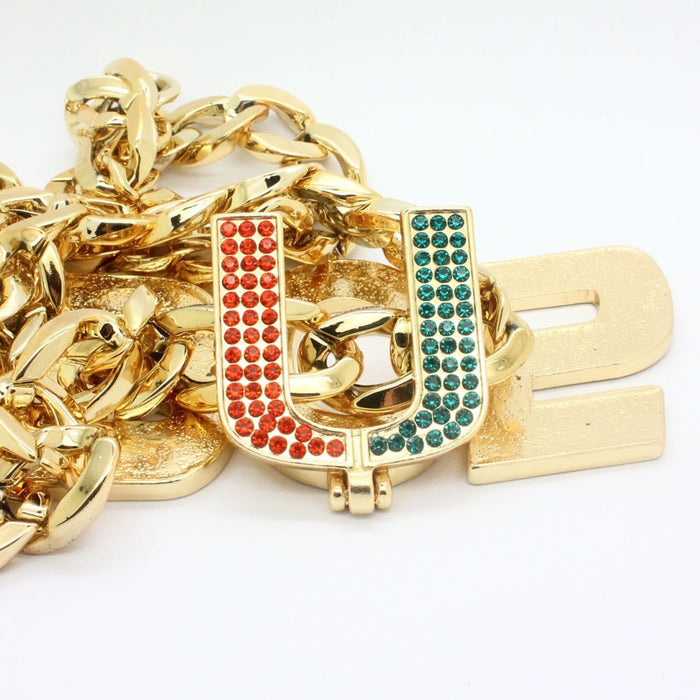 A chunky gold Cuban link chain necklace with a large gold initial pendant spelling 'U' embellished with red and green rhinestones, on a white background.