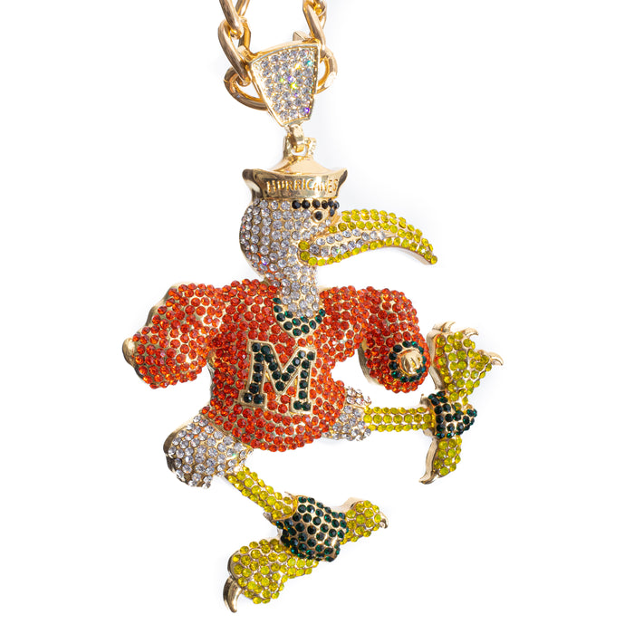 A gold-toned bird mascot pendant, likely a duck or coqui, covered in rhinestones. The bird is wearing an orange jersey with a green and gold letter 'M' on the chest, yellow claws and beak accents, and a gold crown.
