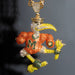 A gold-toned Miami Hurricanes mascot pendant, featuring a running bird covered in orange, yellow, green, and clear rhinestones, with the letter 'M' on its chest and a gold chain attached at the top.