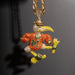 A gold-toned pendant necklace featuring a highly detailed, rhinestone-encrusted mascot character in orange, yellow, green, and white, suspended from a thick gold chain against a dark gray background.