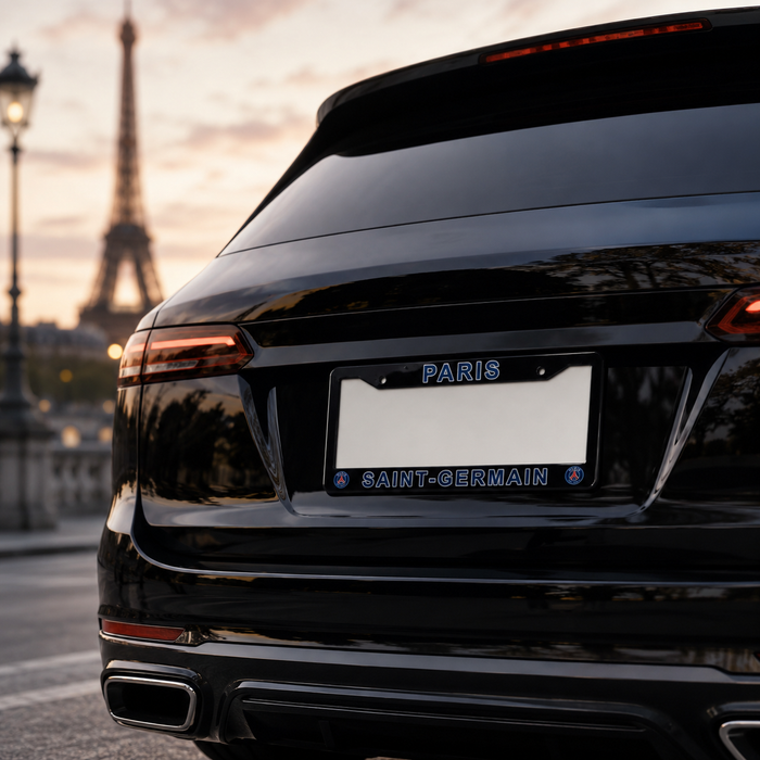 A close-up rear view of a glossy black SUV parked outdoors in Paris, with the Eiffel Tower blurred in the background. The vehicle has a custom license plate frame holding a white plate with blue text reading 'PARIS' at the top and 'SAINT-GERMAIN' at the bottom.