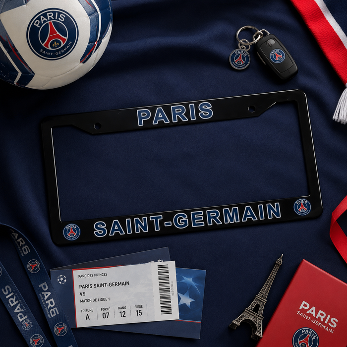A Paris Saint-Germain license plate frame in black with blue and white lettering, displayed in a flat-lay arrangement with a Paris football ball, car key fob, lanyard, ticket, red notebook, and Eiffel Tower charm on a navy blue fabric background.