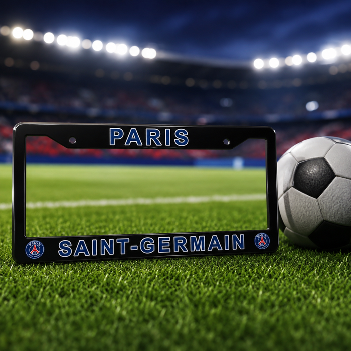A black Paris Saint-Germain license plate frame on a green soccer field, with a soccer ball next to it and a blurred stadium background.