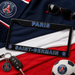A black license plate frame with blue and white Paris Saint-Germain branding, styled on a red, white, and blue Paris scarf with sunglasses, keys, a soccer ball, and a Paris crest charm.