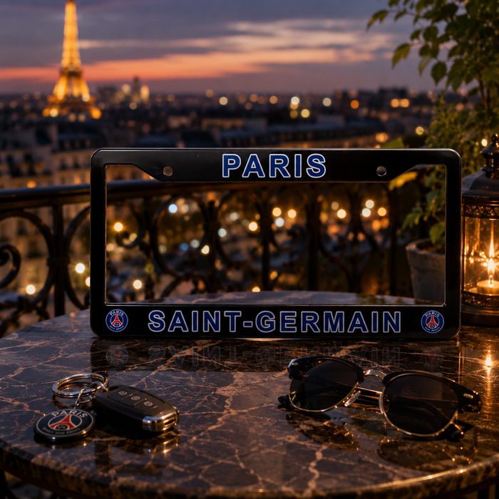 A black license plate frame with 'PARIS' at the top and 'SAINT-GERMAIN' at the bottom, displayed on a dark marble table with sunglasses, keys, and a car key fob. The background shows a blurred Paris cityscape at dusk with the Eiffel Tower and warm bokeh lights.