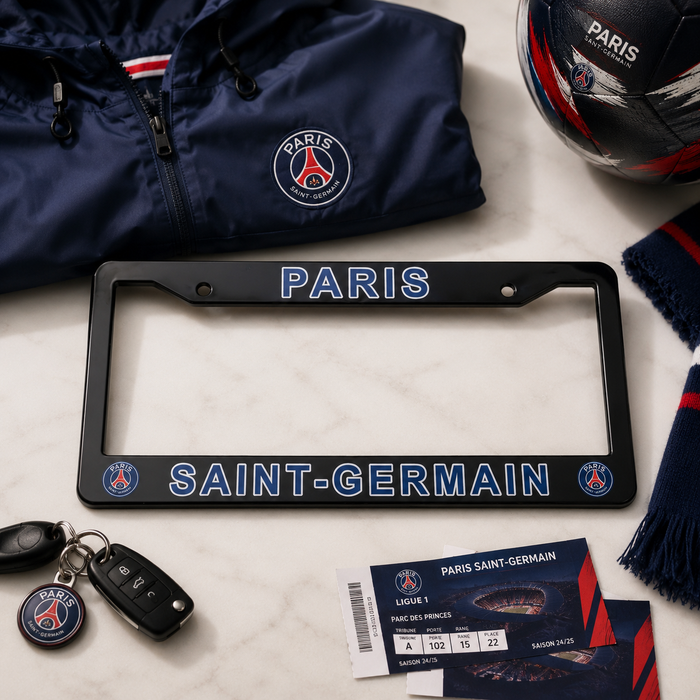 A Paris Saint-Germain license plate frame in black with blue and red lettering, styled in a flat lay with a navy jacket, soccer ball, keys, scarf, and tickets on a white marble background.